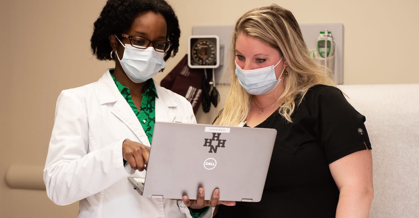 Two masked health care providers reviewing information on a laptop